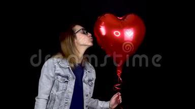 一个年轻的女人以心脏的形式亲吻一个充气气球。 一个在黑色气球上装满氦气的女人